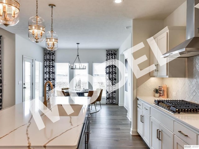 kitchen with stainless steel gas stovetop, white cabinets, hanging light fixtures, wall chimney exhaust hood, and an island with sink