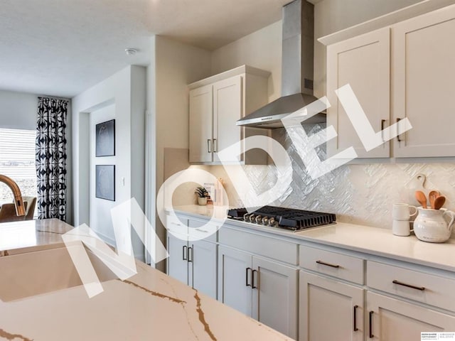 kitchen featuring backsplash, wall chimney exhaust hood, stainless steel gas cooktop, sink, and white cabinets