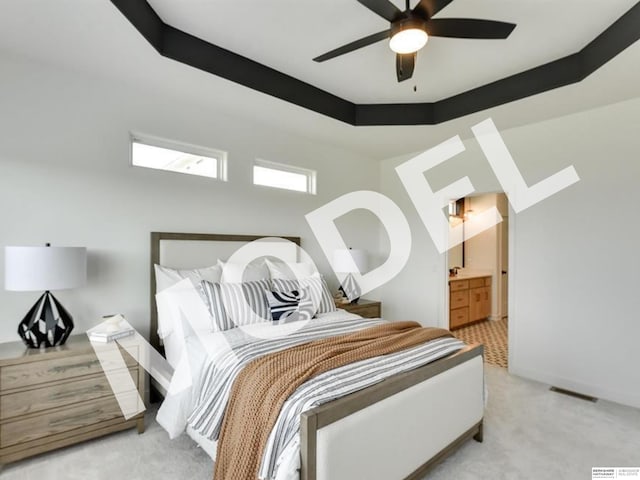 carpeted bedroom with a raised ceiling, ensuite bath, and ceiling fan