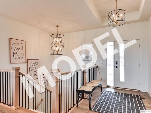 entrance foyer with a raised ceiling, wood-type flooring, and an inviting chandelier