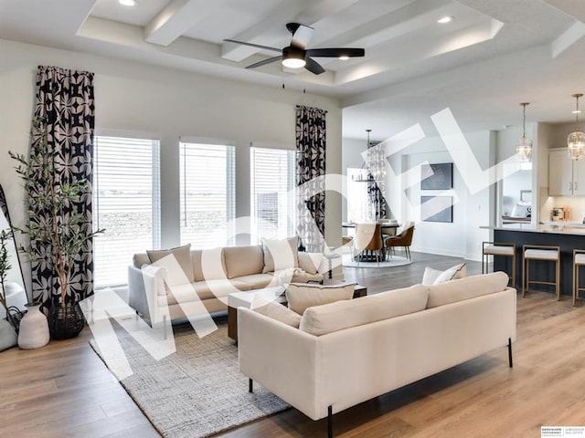 living room featuring ceiling fan with notable chandelier, light hardwood / wood-style floors, and a raised ceiling