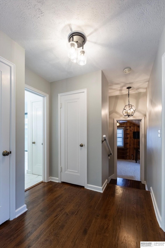 hallway with a textured ceiling, dark wood-type flooring, and a notable chandelier