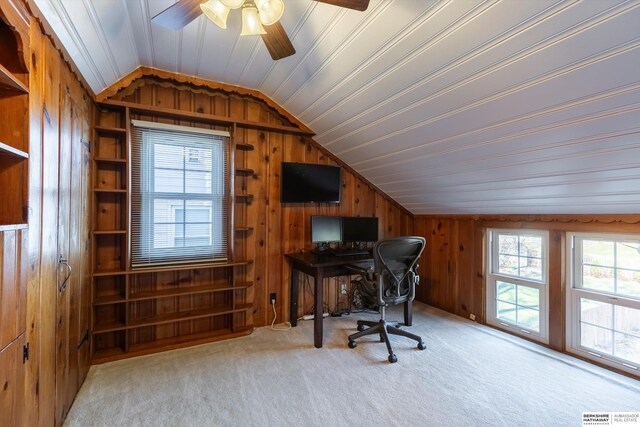 home office with light carpet, wooden walls, ceiling fan, and a healthy amount of sunlight