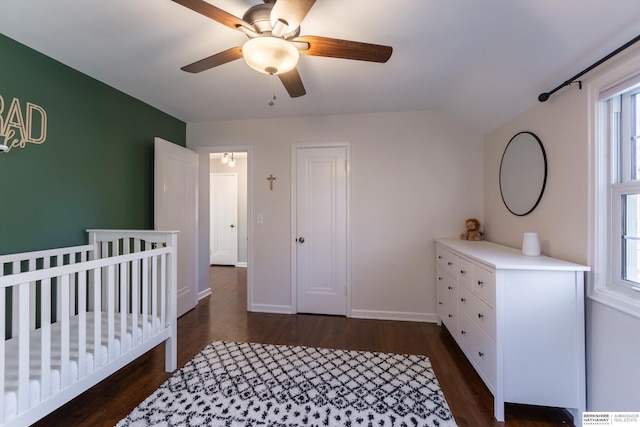 bedroom with a nursery area, multiple windows, dark wood-type flooring, and ceiling fan