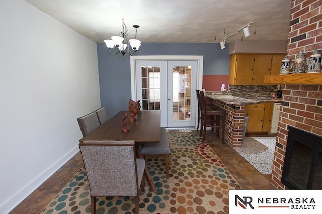 dining area featuring rail lighting, a brick fireplace, an inviting chandelier, and french doors