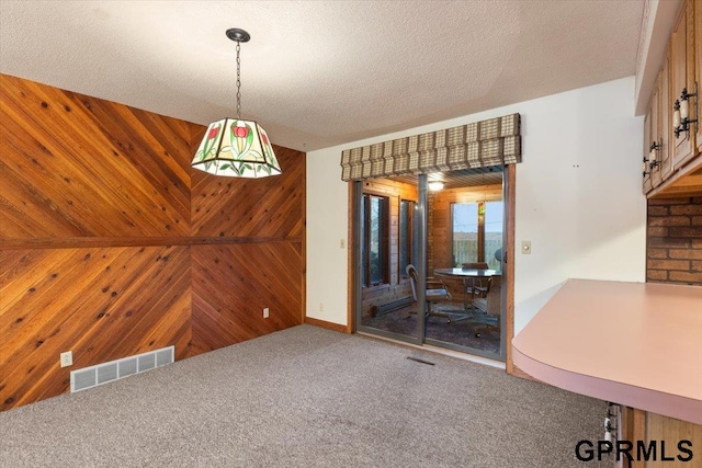 unfurnished dining area featuring carpet floors, a textured ceiling, and wooden walls