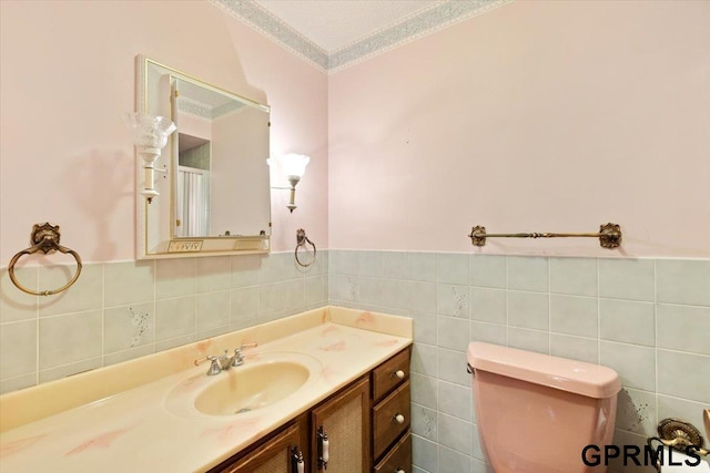 bathroom with vanity, a textured ceiling, crown molding, tile walls, and toilet