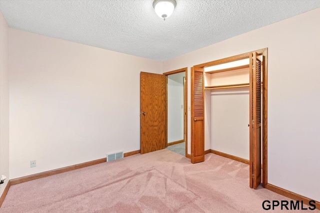 unfurnished bedroom featuring light colored carpet, a textured ceiling, and a closet