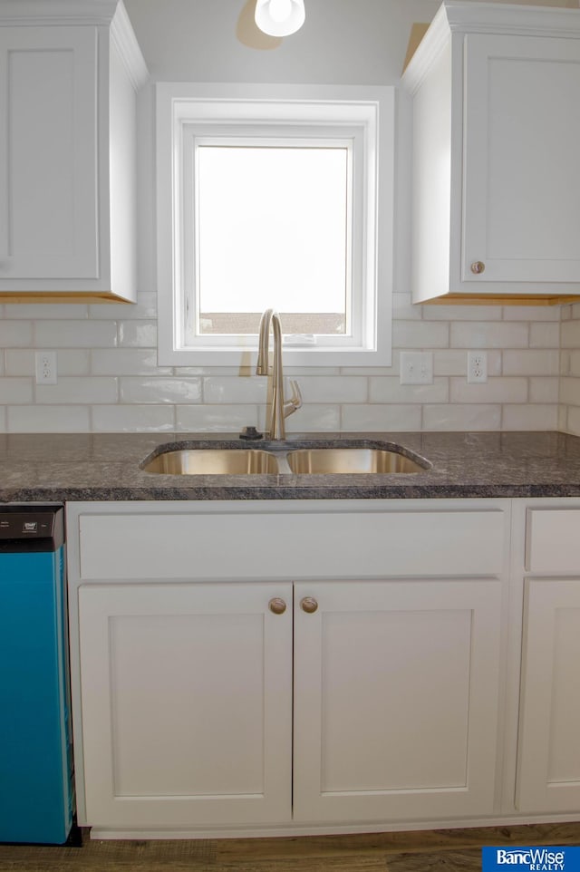 kitchen with white cabinetry, dark stone counters, dishwashing machine, and sink