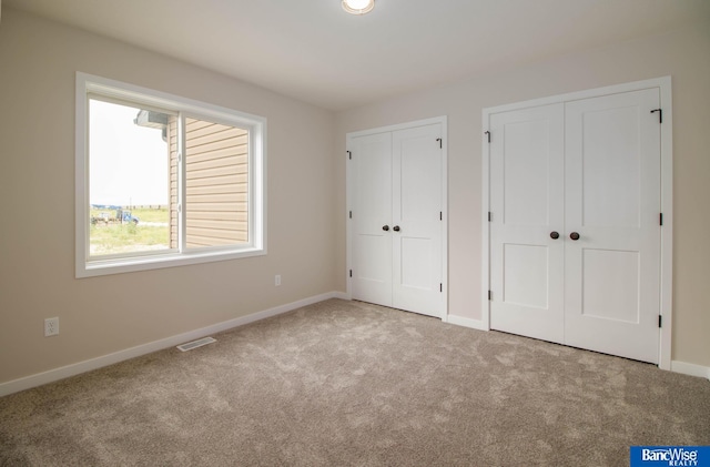 unfurnished bedroom featuring light colored carpet and multiple closets