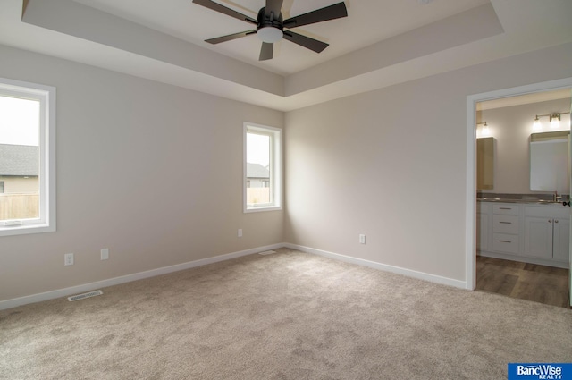 unfurnished bedroom with ensuite bathroom, a tray ceiling, sink, and light carpet