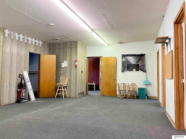 interior space with carpet flooring, a textured ceiling, and wooden walls