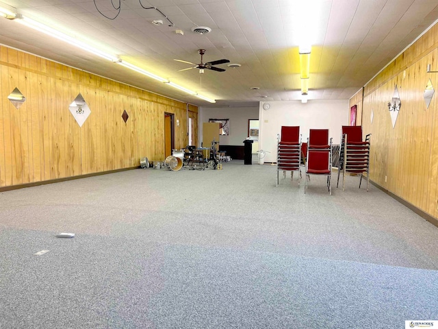 interior space with carpet flooring, ceiling fan, and wood walls