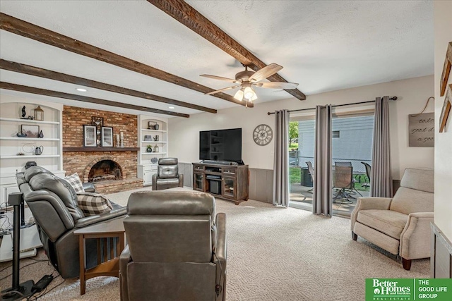 carpeted living room featuring beam ceiling, built in shelves, ceiling fan, a textured ceiling, and a fireplace