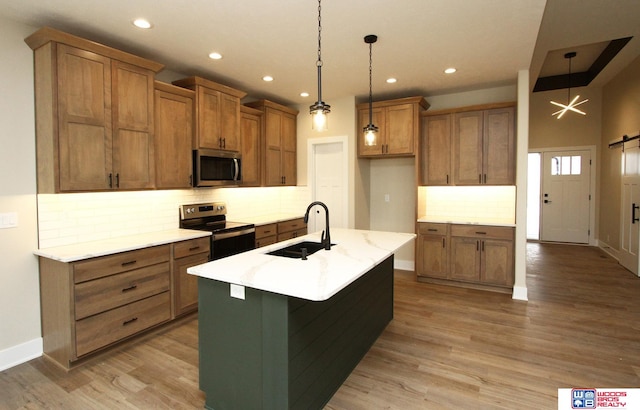 kitchen with stainless steel appliances, sink, a barn door, decorative light fixtures, and an island with sink