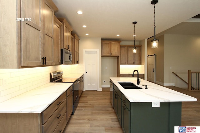 kitchen with stainless steel appliances, a kitchen island with sink, sink, light hardwood / wood-style floors, and hanging light fixtures