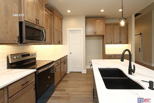 kitchen with sink, stainless steel appliances, a barn door, light hardwood / wood-style floors, and decorative light fixtures