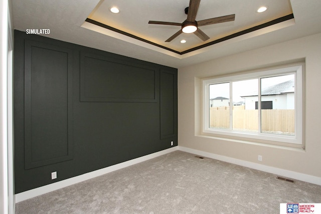 carpeted spare room featuring a raised ceiling and ceiling fan