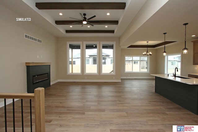 unfurnished living room featuring ceiling fan with notable chandelier, a raised ceiling, light wood-type flooring, and sink