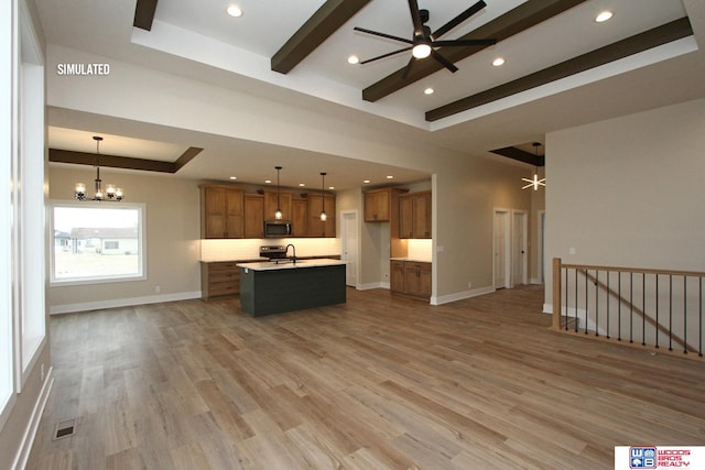 kitchen featuring sink, hanging light fixtures, light wood-type flooring, an island with sink, and a tray ceiling