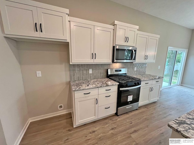 kitchen featuring tasteful backsplash, light stone counters, stainless steel appliances, white cabinets, and light hardwood / wood-style floors