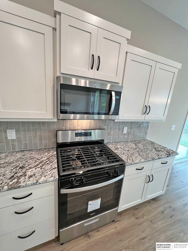 kitchen with decorative backsplash, light hardwood / wood-style flooring, white cabinets, and appliances with stainless steel finishes