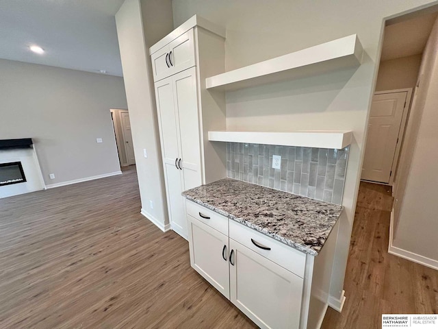 kitchen with white cabinets, light stone countertops, light hardwood / wood-style flooring, and tasteful backsplash