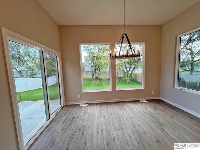 unfurnished dining area with a chandelier, plenty of natural light, and hardwood / wood-style floors