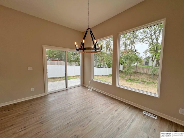 unfurnished dining area featuring wood-type flooring, a wealth of natural light, and a notable chandelier