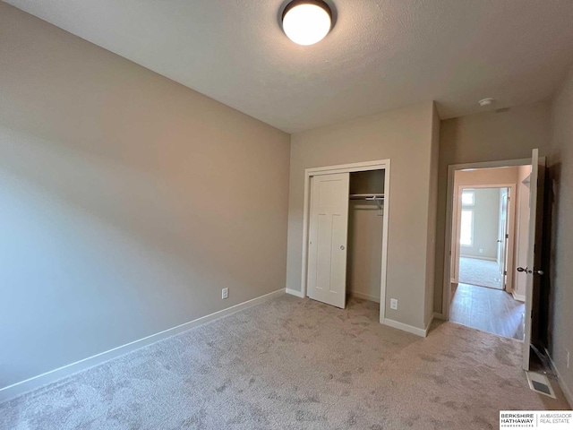 unfurnished bedroom with light carpet, a textured ceiling, and a closet