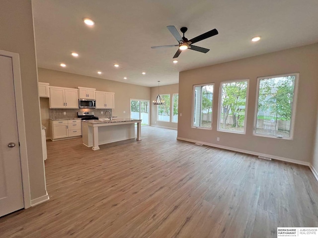 kitchen with stainless steel appliances, a center island with sink, light hardwood / wood-style floors, white cabinetry, and hanging light fixtures