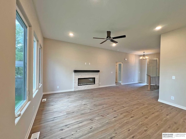 unfurnished living room featuring ceiling fan with notable chandelier, light hardwood / wood-style floors, and a fireplace