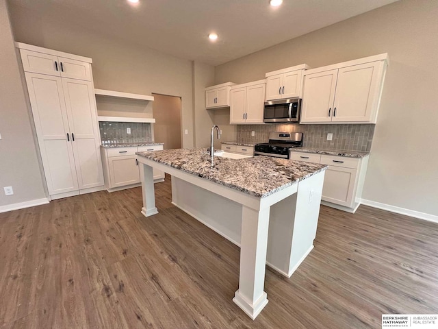 kitchen featuring sink, light stone counters, dark hardwood / wood-style floors, a center island with sink, and appliances with stainless steel finishes