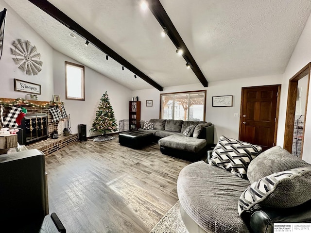 living room featuring hardwood / wood-style floors, lofted ceiling with beams, a textured ceiling, and a brick fireplace