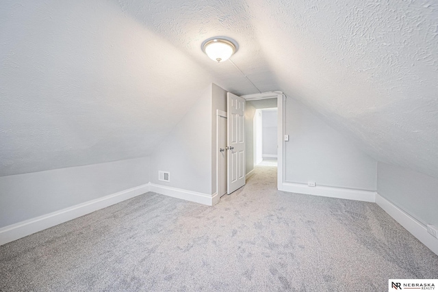 additional living space featuring lofted ceiling, light colored carpet, and a textured ceiling