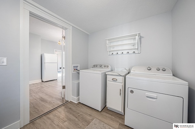 washroom featuring cabinets, a textured ceiling, light hardwood / wood-style flooring, and washing machine and dryer