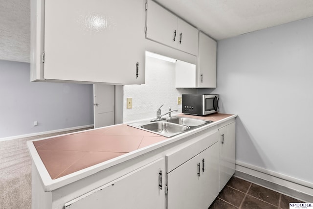 kitchen with dark tile patterned flooring, white cabinetry, sink, and a textured ceiling