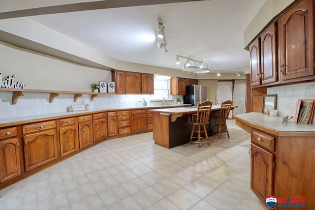 kitchen with a kitchen bar, stainless steel refrigerator, decorative backsplash, and a center island