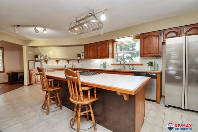 kitchen with a center island, sink, appliances with stainless steel finishes, tile counters, and a kitchen bar