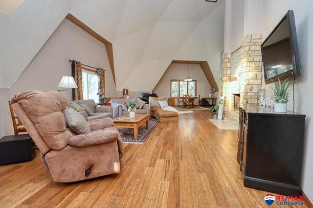 living room with a stone fireplace, a chandelier, light hardwood / wood-style floors, and lofted ceiling