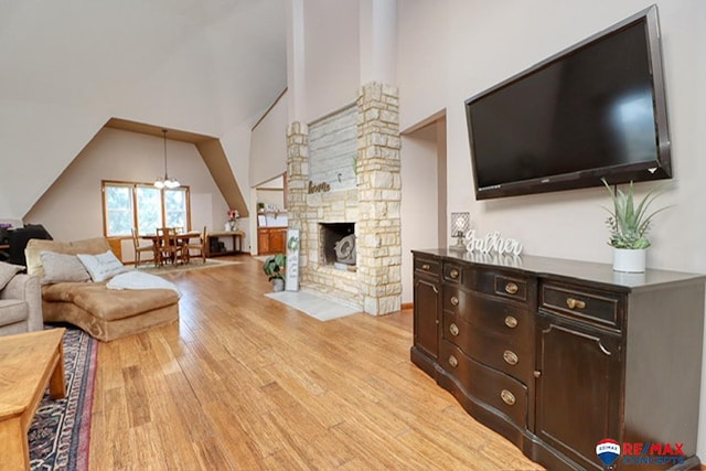 living room with a chandelier, high vaulted ceiling, light hardwood / wood-style flooring, and a stone fireplace