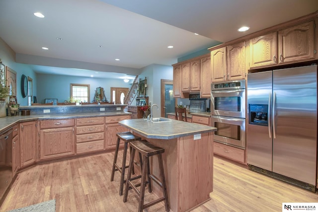 kitchen with a kitchen island with sink, a kitchen breakfast bar, sink, light hardwood / wood-style flooring, and appliances with stainless steel finishes