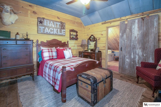 bedroom featuring wood-type flooring, wooden walls, ceiling fan, and lofted ceiling