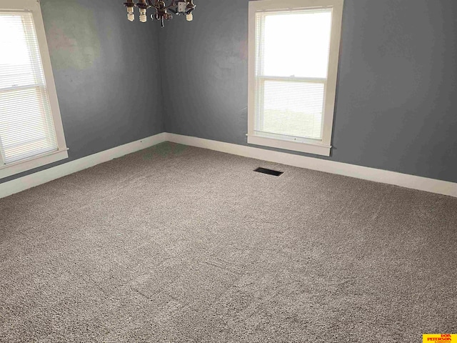 carpeted empty room with plenty of natural light and an inviting chandelier