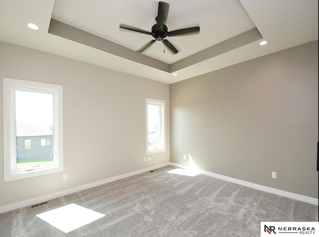 empty room featuring carpet flooring, a tray ceiling, and ceiling fan