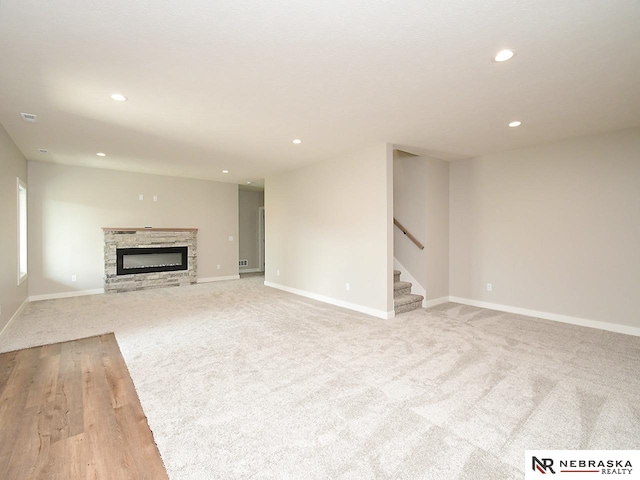 unfurnished living room featuring a stone fireplace and light colored carpet