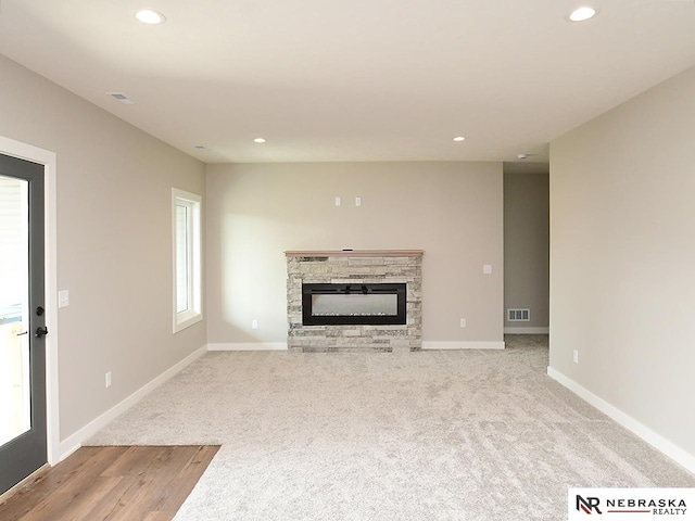 unfurnished living room featuring a stone fireplace and light carpet