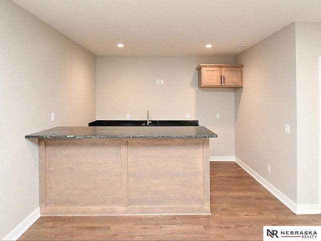 kitchen featuring sink, light hardwood / wood-style flooring, dark stone countertops, light brown cabinetry, and kitchen peninsula