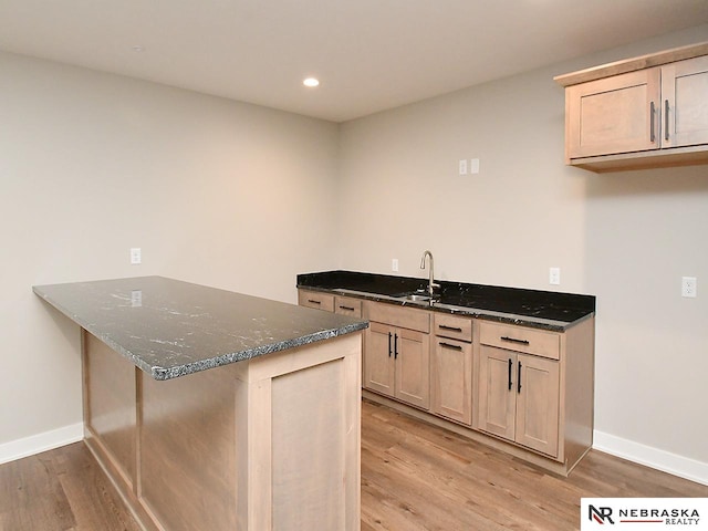 kitchen featuring kitchen peninsula, light brown cabinets, light wood-type flooring, and dark stone countertops