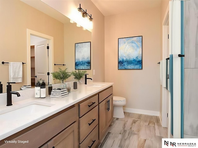 full bathroom featuring baseboards, a sink, toilet, and double vanity